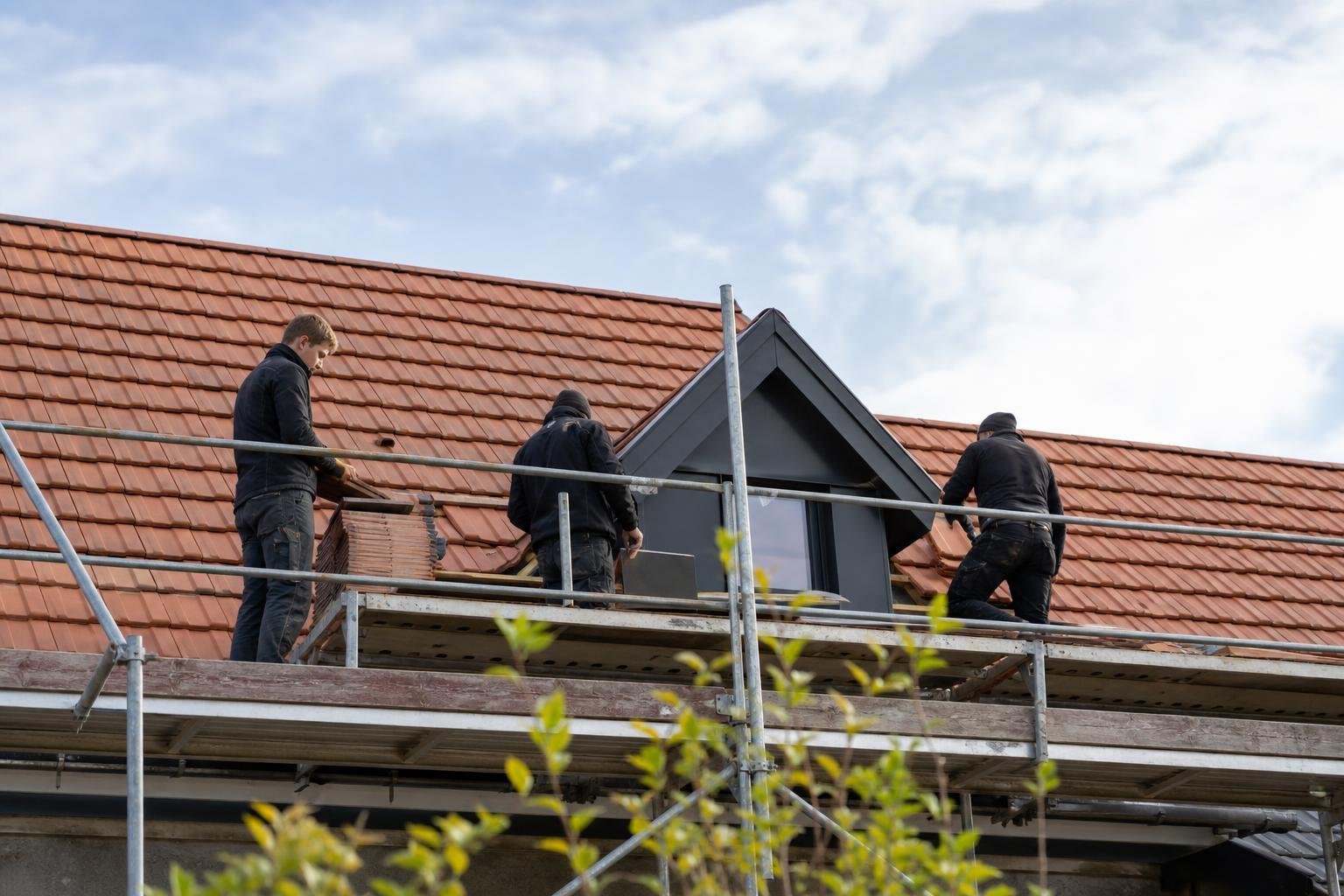 Équipe de couvreurs sur un échafaudage devant une toiture en tuiles